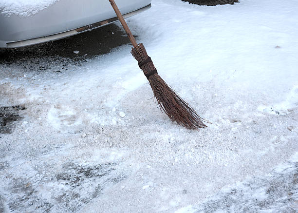 A broom clears snow off a driveway as dawn begins to break.
