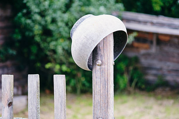 A weathered metal cooking pot is overturned on a wooden fence post. The setting shows a rural or agricultural atmosphere during the daytime.