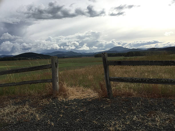 Foothills of the Oregon Coast Mountain range with moody clouds overhead and framed by a split rail fence