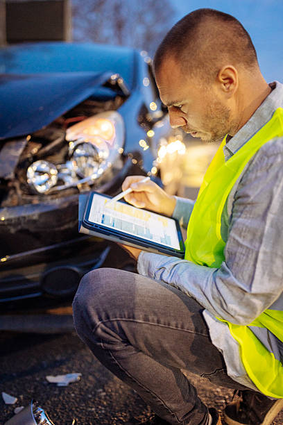 istock Man in Safety Vest Inspecting Car Accident with Tablet 2231052606