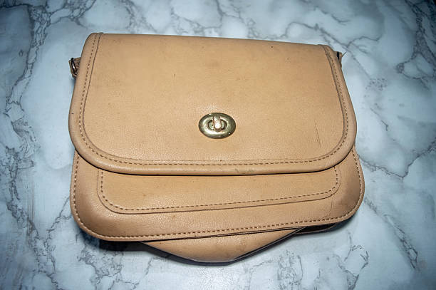 Tan leather cross body bag featuring a turn lock closure, shown on a marble surface. A stylish accessory, perfect for everyday use and fashion forward individuals.