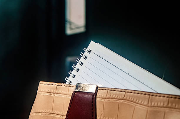 istock Close up shows a notebook with lines inside a beige purse with a brown strap and metal clasp, set against a dark backdrop. The scene evokes organization and style 2231056736