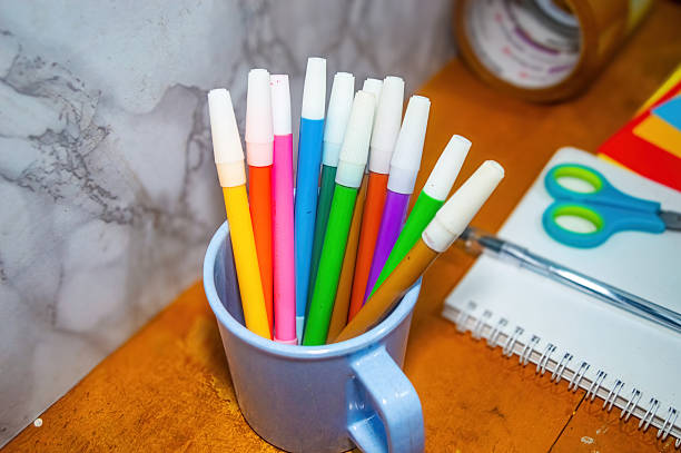 istock Overhead shot displays a cup filled with colorful markers, alongside a notebook and scissors, set on a wooden table, perfect for illustrating creative workspace 2231059435