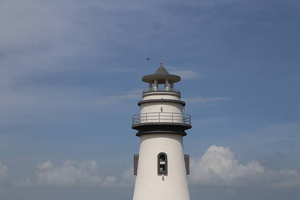 A tall white lighthouse with a black roof. The lighthouse is on a cloudy day. There are birds flying around the lighthouse
