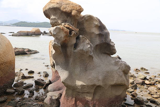A large rock with a hole in the middle. The rock is on the beach. The water is calm