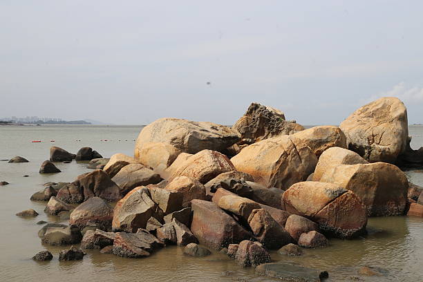 A large pile of rocks is on the beach. The rocks are brown and gray. The water is calm