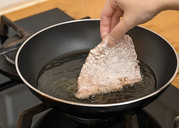 Family working together in a modern kitchen, preparing a Tuscan Chicken meal. Close-up teenage boy adding meat to a frying pan. Chicken fillets dredged are being fried on olive oil. Shot with Canon R5