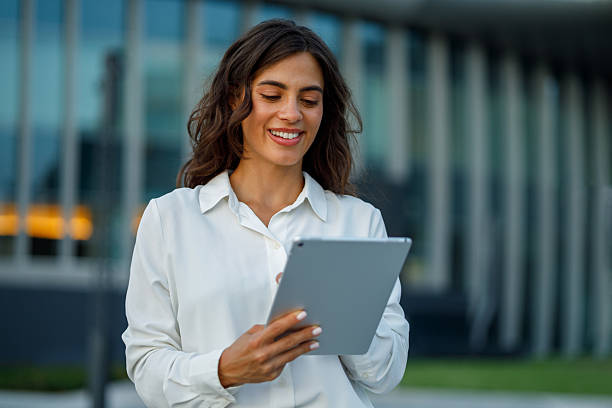 istock Young businesswoman smiling while using a digital tablet, standing confidently in front of a modern office building in an urban setting 2231068726