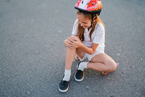istock A girl wearing a helmet crying while touching her knee after falling off a skateboard on an asphalt road. 2231071472