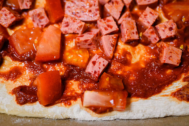 Neapolitan-style homemade pizza: sausage cubes and fresh tomatoes before baking.