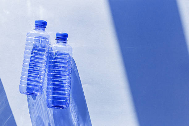 istock Clear plastic water bottles for clean water on white blue background closeup, minimal aesthetic lifestyle photo, top view, flat lay, Naural light, sunlight shadows, caustic light effect, star filter 2231074232
