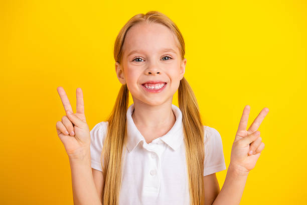 istock Cheerful young girl on a yellow background displaying peace gestures with both hands, showcasing joy and positivity 2231074344
