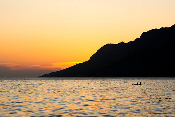 Sunset on the Croatian coast of the Adriatic Sea, with two rowers in the distance in the frame.