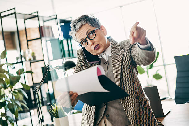 istock Mature professional woman multitasking in an office environment holding documents while pointing and speaking on the phone 2231075349