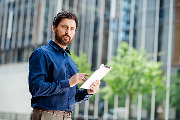 istock Handsome young businessman using tablet outdoors in an urban business district with focus on modern digital solutions 2231077110