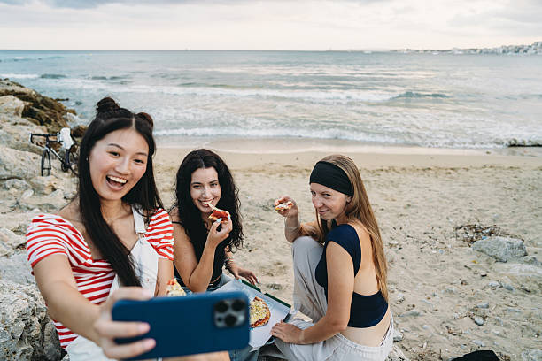 istock Young women taking selfie while eating pizza at the beach 2231079032