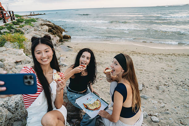 istock Young women taking selfie while eating pizza at the beach 2231079034