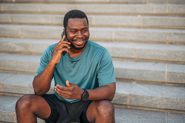 istock Smiling black athlete relaxing on steps while talking on phone 2231079750