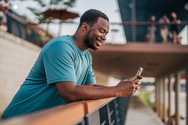 istock Young man smiling and using his smartphone leaning on a railing 2231080604