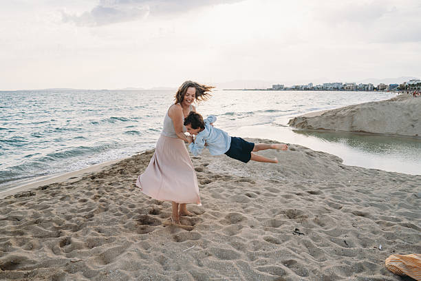 istock Mother swinging her son on a sandy beach 2231081531