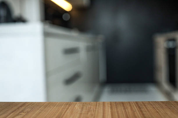 istock Wooden tabletop with blurred modern kitchen interior in the background. Soft lighting from under-cabinet LED strip highlights the minimalist black and white cabinetry 2231082504