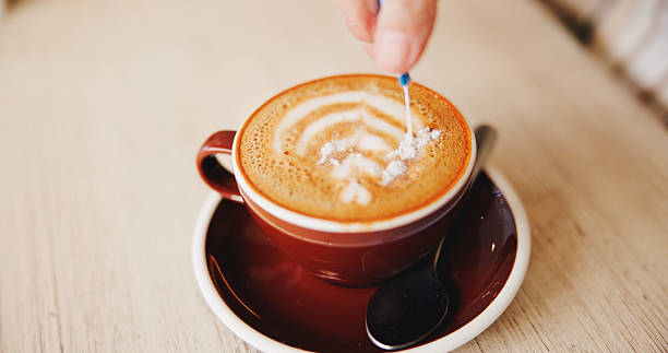 istock Table, hands and sugar in cappuccino at restaurant for caffeine, prepare beverage and warm drink. Diner, person and sachet for coffee sweetener, espresso break and morning routine to enhance flavor 2231083610