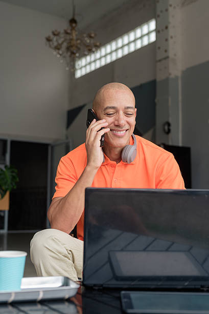 istock Bald Hispanic man sitting and using laptop computer and phone in coffee shop restaurant 2231084728