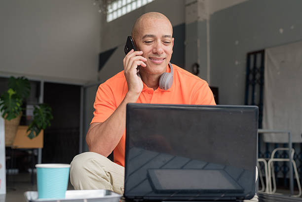 istock Bald Hispanic man sitting and using laptop computer and phone in coffee shop restaurant 2231084758