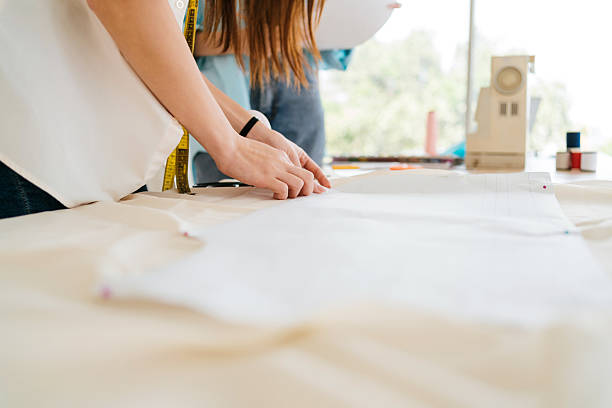 istock Fashion designer tailoring and sewing in a bright workshop, cutting fabric with patterns, textiles, and tools. Handmade craft, dressmaking, and maker skills shown with sewing machine. 2231086907