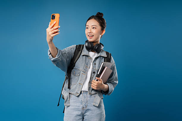 istock A cheerful student captures a selfie with her mobile phone holding books against a blue backdrop 2231090401