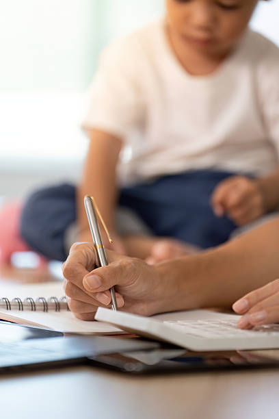 istock Financial Skills Development. A mother writes notes while her child plays with a piggy bank. 2231091326