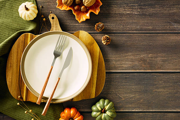 istock Thanksgiving dinner table setting with empty plate, cutlery, decorative pumpkins candles, pine cones on rustic wooden table. Top view, Flat lay. 2231096276