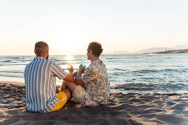 istock Two men are enjoying drinks by the beach during a beautiful sunset. 2231099852