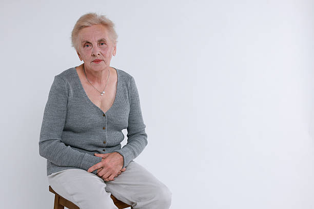 Mature woman looking away while sitting on a stool in a studio. Mature woman with short grey hair and eyeglasses wearing casuals looking away in studio.