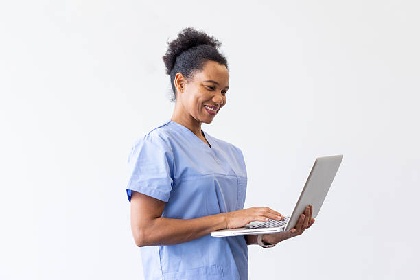 istock Happy female doctor wearing blue scrubs using laptop computer, standing against white background 2231106449