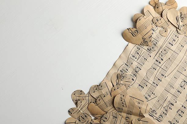 Paper hearts with notes and musical note sheet on white wooden table, flat lay. Space for text