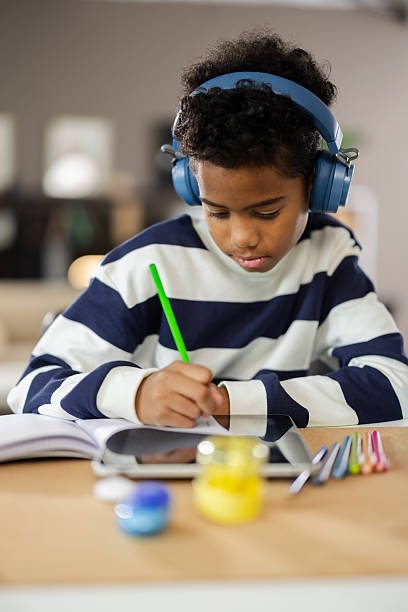 istock Young boy wearing headphones writing and studying at home 2231111108