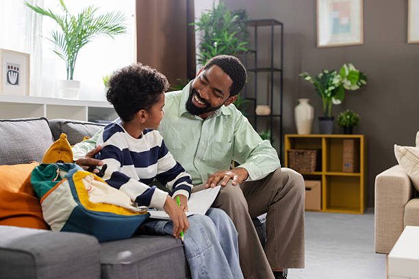 istock Happy african american father helping son with homework on sofa at home 2231111152