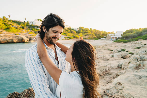 istock Young couple embracing on a rocky beach at sunset 2231111875