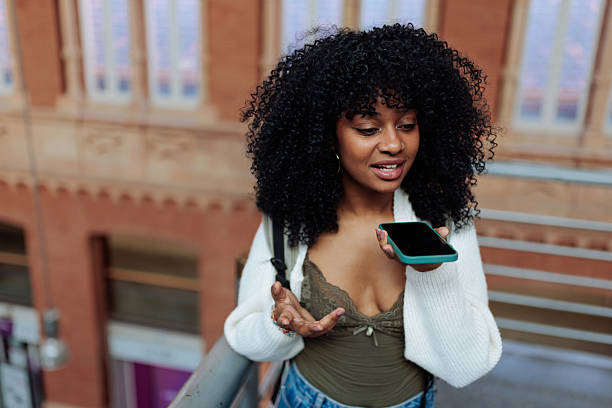 Young student sending a voice message on her smart phone while gesturing in a modern building
