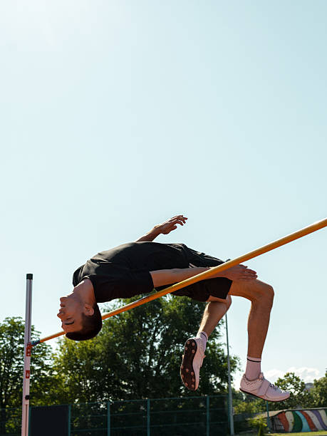 Sportsman high jumping through pole and falling on exercise mat while training in gym wide angle view