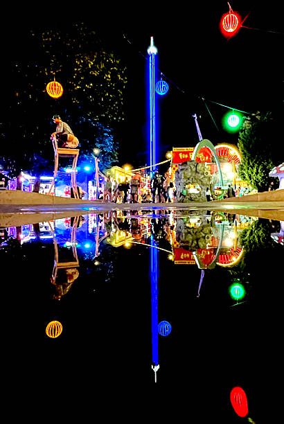 istock Night View of Amusement Park Lights Reflected in Large Puddle Creating Symmetrical Effect 2231126687