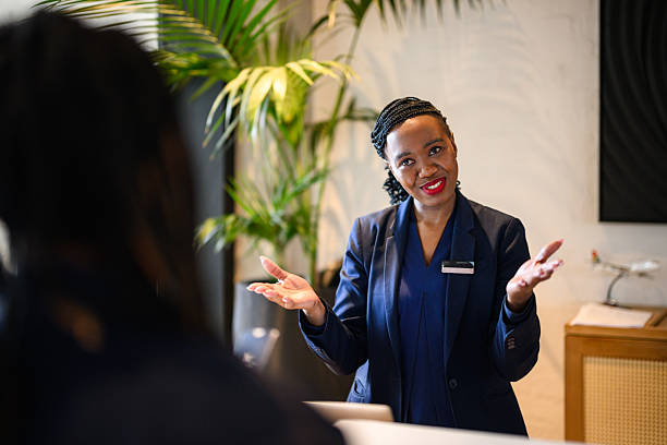 Receptionist engaging with hotel guests across the check in counter, framed by modern lobby decor and tall green plants inside a contemporary five star setting.