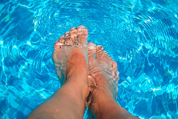 Legs and feet dangling in a refreshing, crystal-clear swimming pool on a sunny day, creating a relaxing and enjoyable summer vacation atmosphere