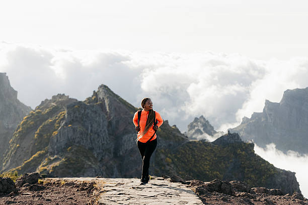 Young hiker with long braids walking on a hiking trail with a dramatic view of the mountains behind her