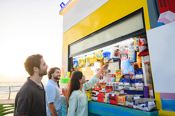 Side view of multiracial men and women friends selecting snacks from shop on Jeddah Corniche waterfront. Saudi Arabia, Middle East.