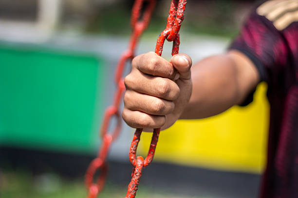 a child's hand holding onto a red metal chain, with a blurred background of green and yellow colors, suggesting a fun outdoor activity.