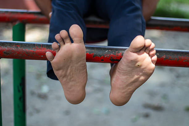 a person's bare feet with toes spread, hanging from a red metal bar, suggesting a moment of rest or play in an outdoor park.