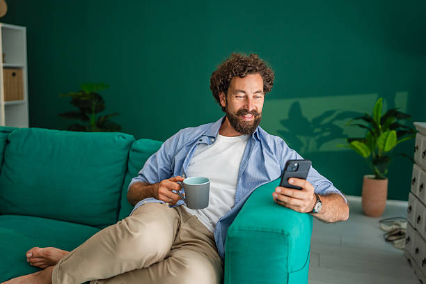 istock Man relaxing on sofa, enjoying coffee and browsing smart phone at home 2231135083