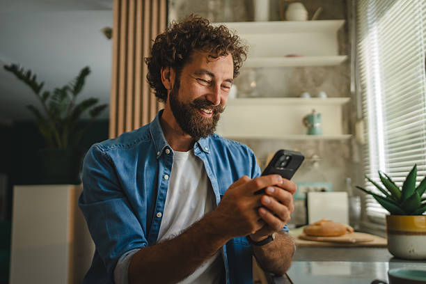 istock Smiling man using smart phone in kitchen reading good news 2231135448